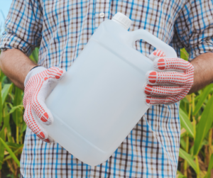 A person wearing gloves, holding an empty plastic pesticide container.