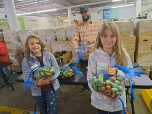 Two girls hold bags of produce at a warehouse.